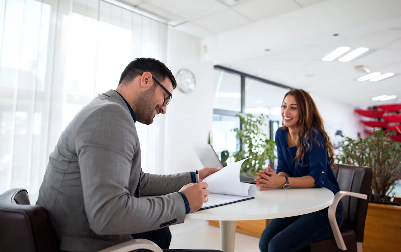 A man and woman discuss documents at a table, demonstrating employability skills in an office setting.