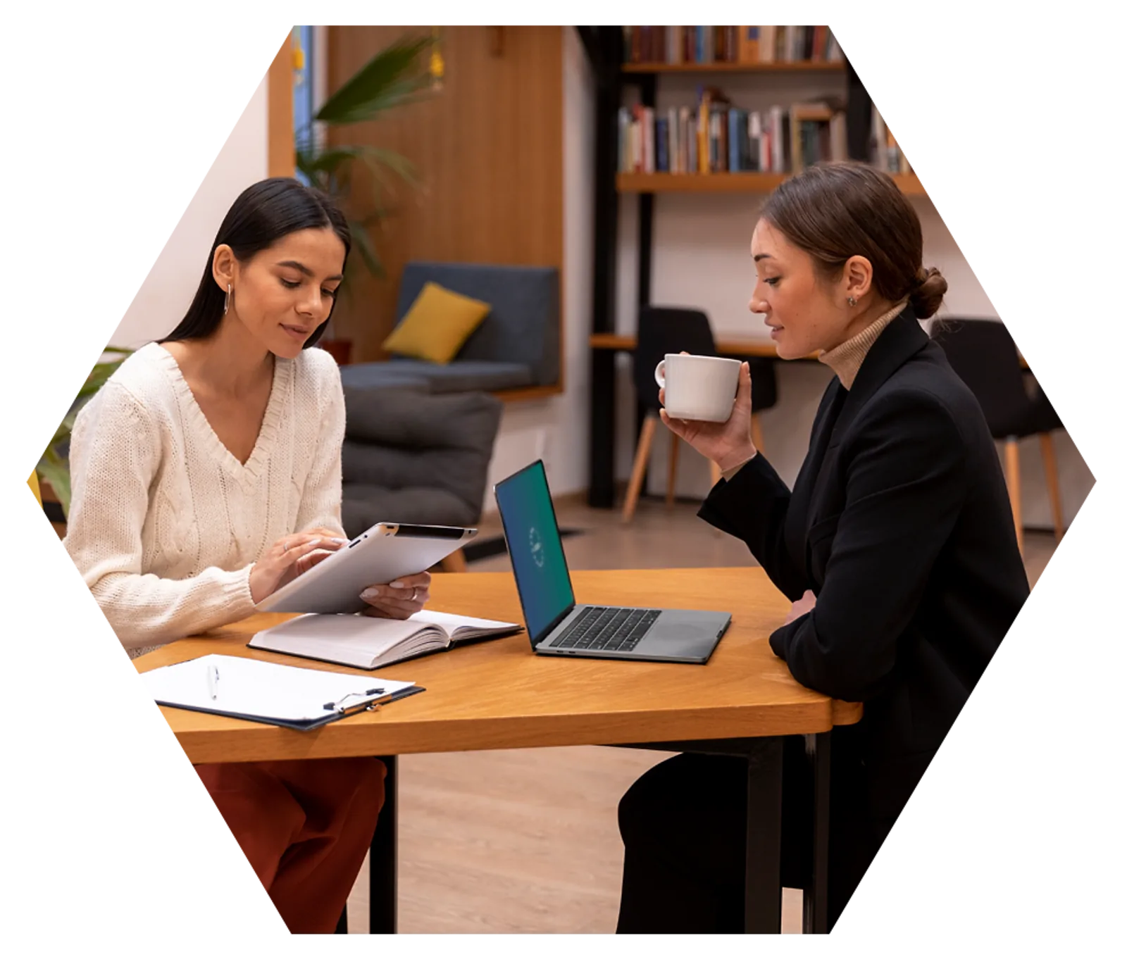 Two women discuss work at a table with a laptop, demonstrating CAQA LLND's focus on employability skills.